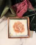 Load image into Gallery viewer, Small framed artwork of a camelia on a marble surface with green fabric and red ribbon by Meredith Raiford Akins